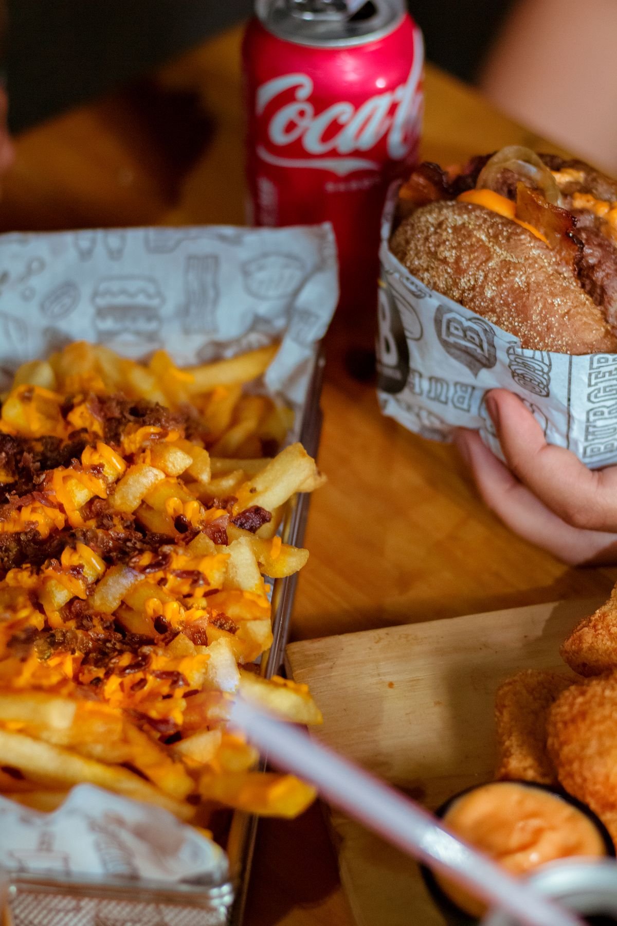 A burger, fries and a cola set out on a table, used as an editorial illustration for “Reading menu prices across the UK, US and Canada”