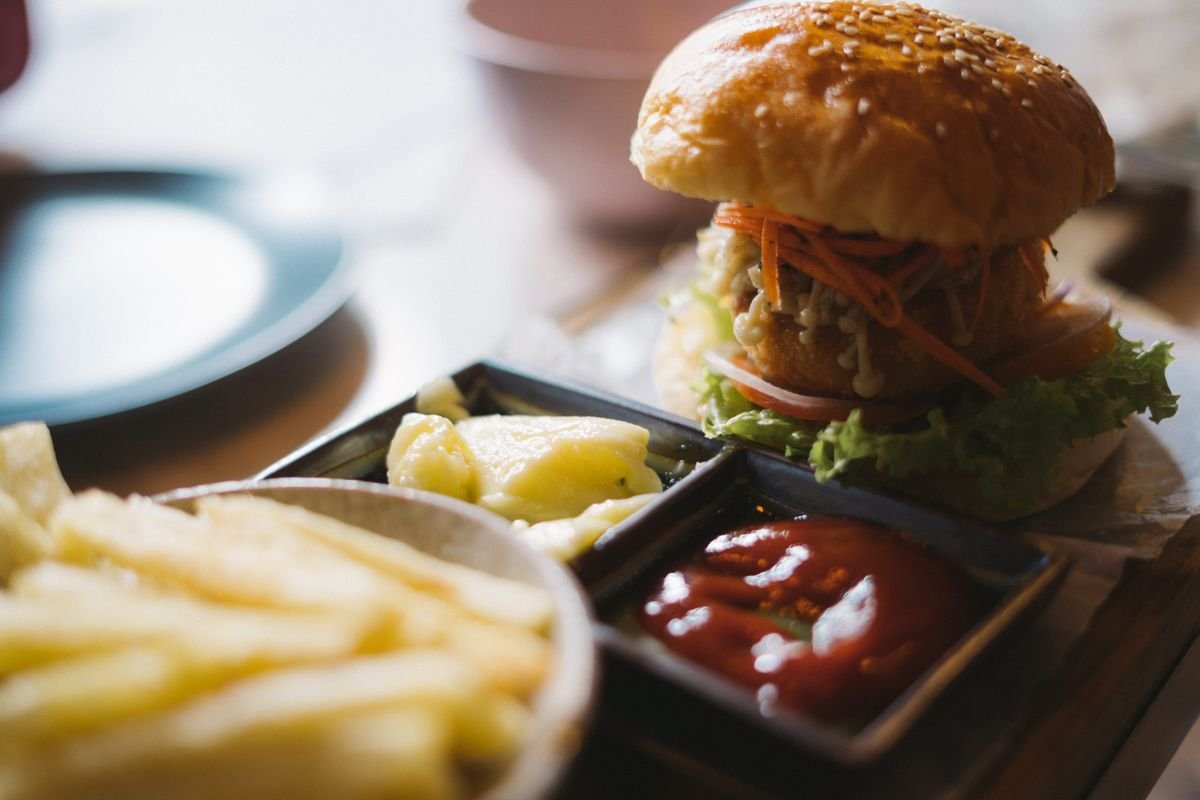 Close-up of a stacked burger with fries and dipping sauces, used as an editorial illustration for “Monster Mac: how fans build a bigger stack”