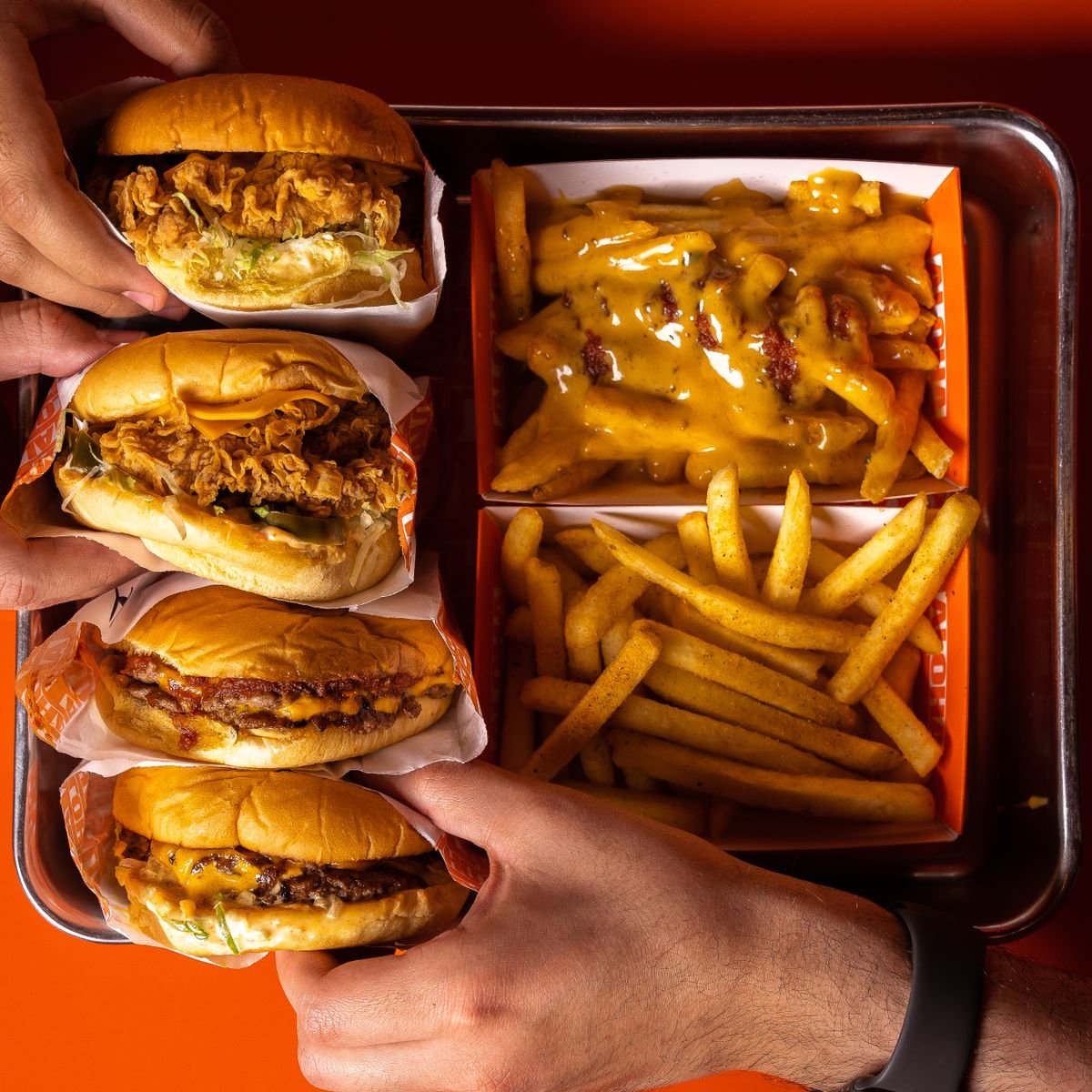 A tray of burgers, cheesy fries and sides seen from above, used as an editorial illustration for “Surf & Turf: pairing a burger with fish”