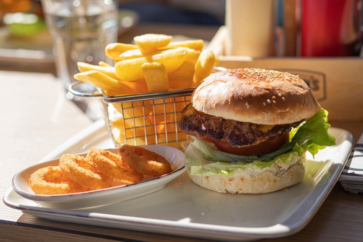 A cheeseburger served with crispy fries and onion rings, used as an editorial illustration for “Poor Man’s Big Mac: a budget-minded riff”