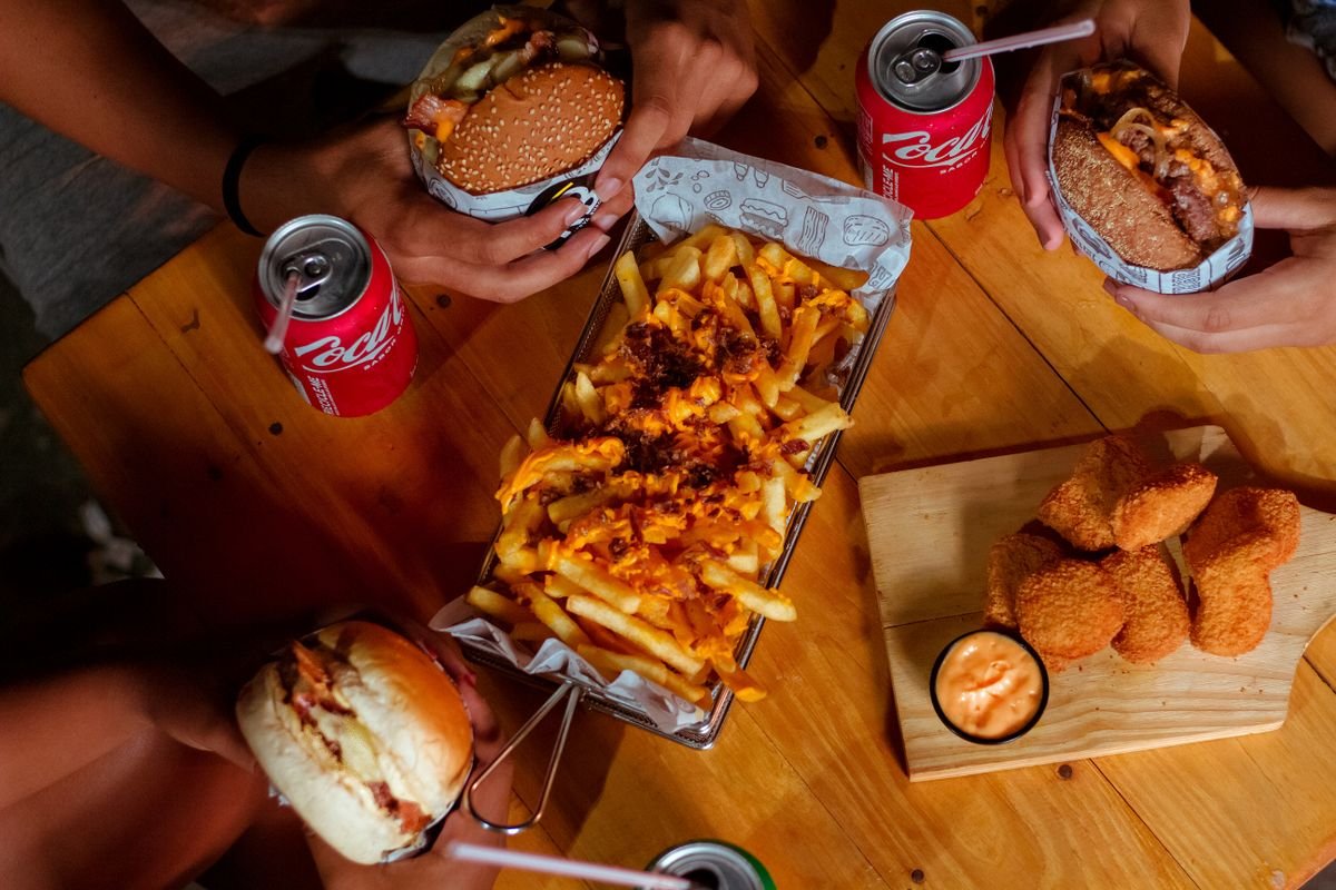 A wooden table with burgers, fries, chicken nuggets and drinks, used as an editorial illustration for “Land, Air & Sea: the three-protein mash-up”