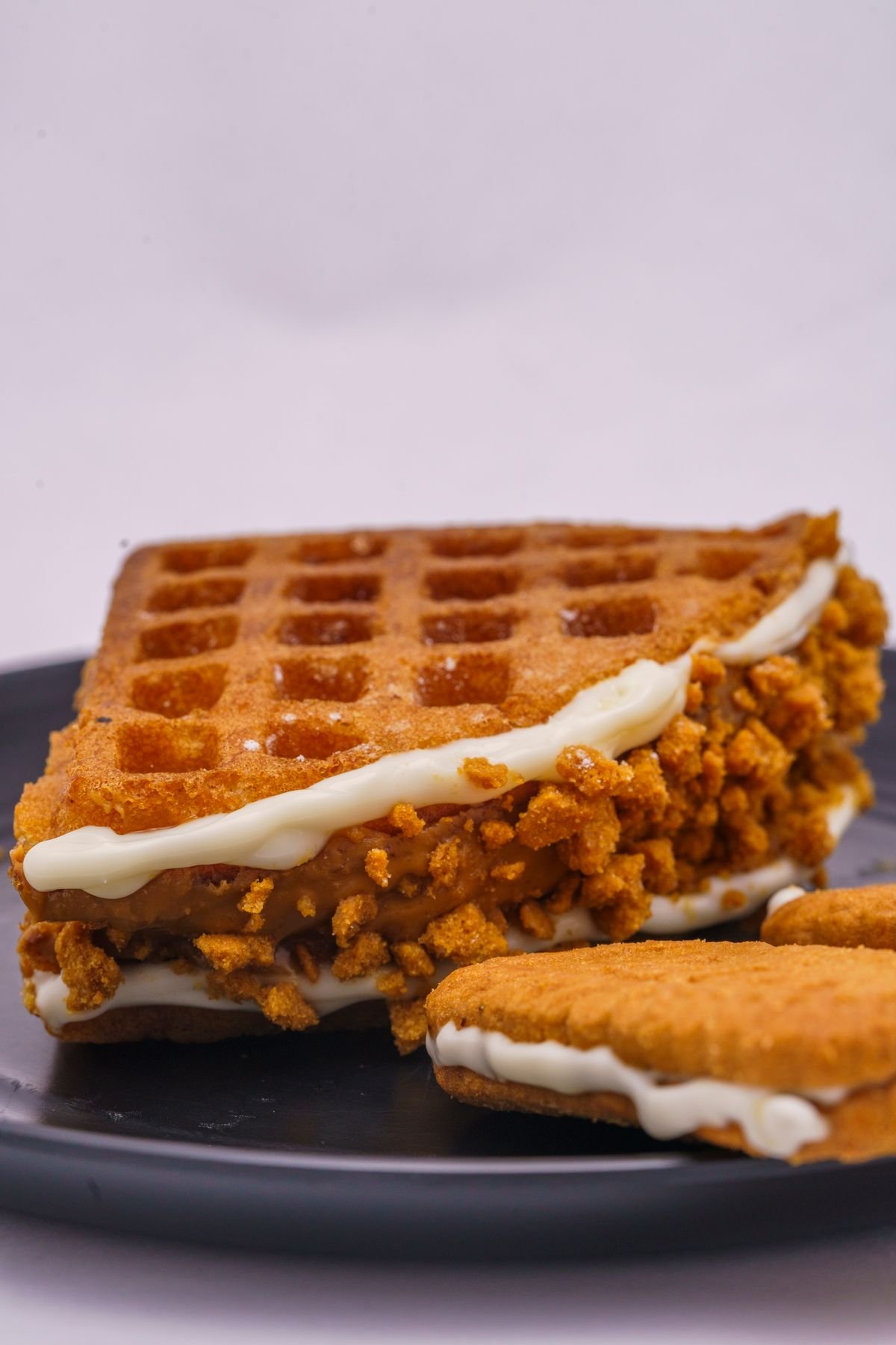A waffle ice cream sandwich with crumbs on a black plate, used as an editorial illustration for “McFlurry Stroopwafel: a Dutch-inspired dessert”