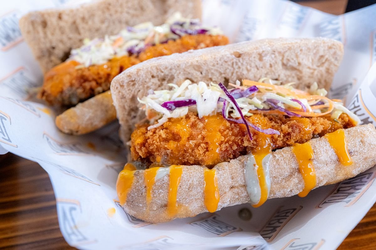 A crispy fried chicken sandwich topped with coleslaw and a spicy drizzle, used as an editorial illustration for “McSpicy: a regional chicken menu guide”