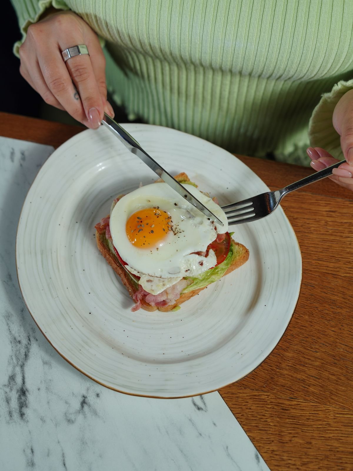 A knife cutting avocado toast topped with bacon and a fried egg, used as an editorial illustration for “A balanced way to think about fast-food nutrition”