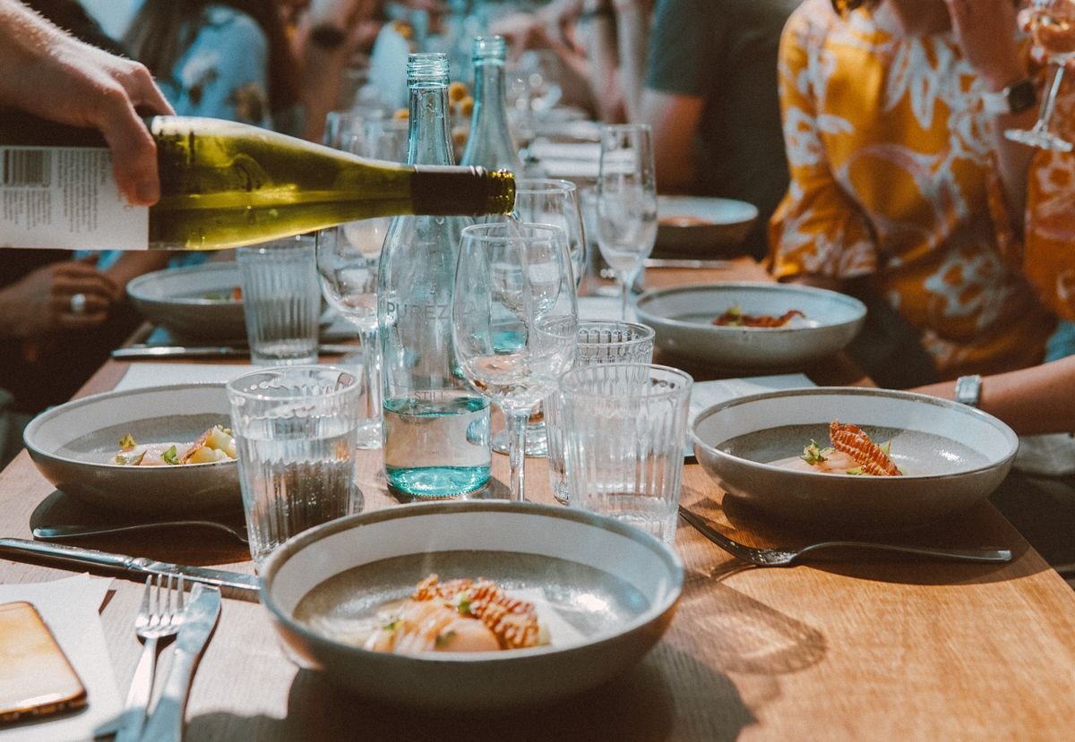 Diners sharing wine and meals at a busy restaurant table in Sydney, used as an editorial illustration for “Australia, Japan and the Eurozone: price context”